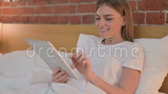 年轻女子在床上使用平板电脑视频的预览图