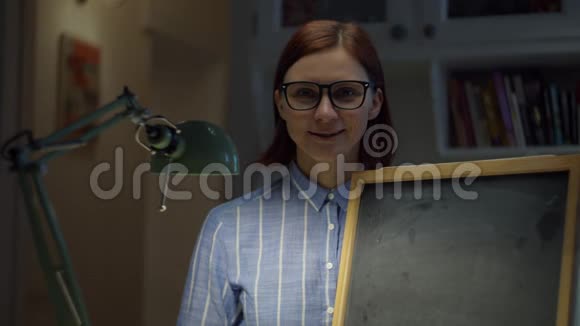 30多岁的女人戴着眼镜拿着空粉笔板在家看着相机在线教育过程网络摄像机视图视频的预览图