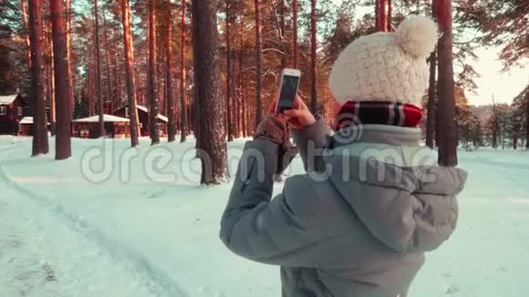 一个漂亮的女孩用手机在森林里的雪村拍照视频的预览图