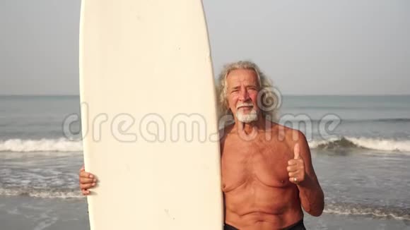 在海滩上有冲浪板的老头竖起大拇指视频的预览图