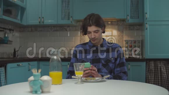 20多岁的年轻人独自在厨房吃饭男的手里拿着手机笑着在家吃晚饭视频的预览图