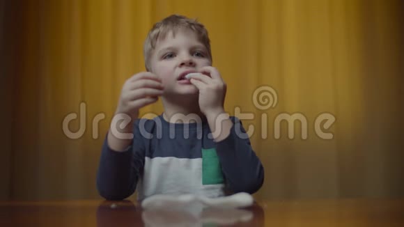 金发男孩在家里的桌子上吃着薯片做着滑稽的食物眼睛男孩喜欢吃零食和玩耍视频的预览图