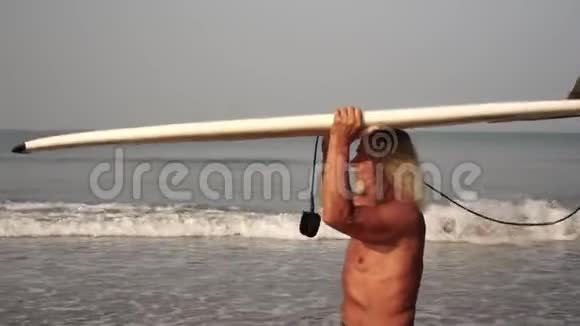 穿着冲浪板在沙滩上运动的老人一个成熟男人的冲浪肖像视频的预览图
