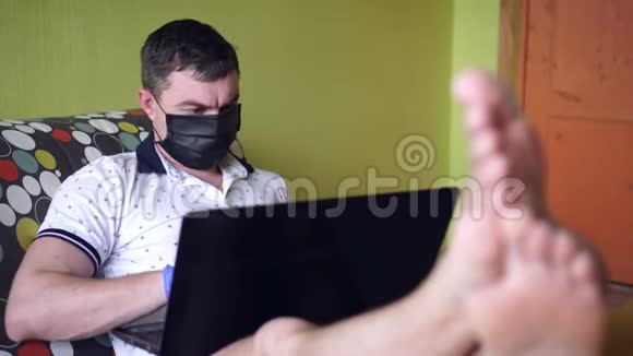 带着笔记本电脑的戴着医疗面具的男人冠状病毒和家庭办公室视频的预览图