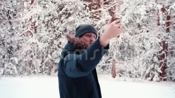 英俊的游客在白雪皑皑的冬林里用手机自拍视频的预览图