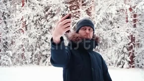 帅哥vlogger在雪林用手机拍摄自拍视频会议视频的预览图