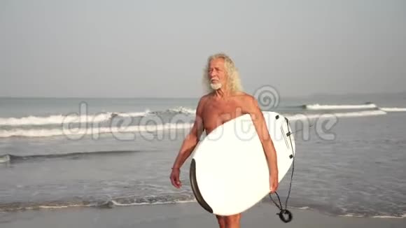 爷爷带着冲浪板在海滩上老年成熟男性冲浪者视频的预览图
