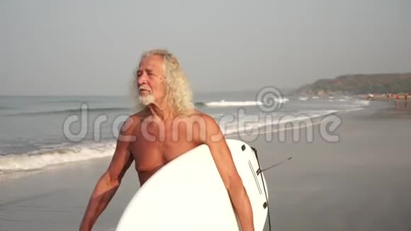 一个成熟的老人带着冲浪板沿着海边散步祖父是个冲浪者视频的预览图