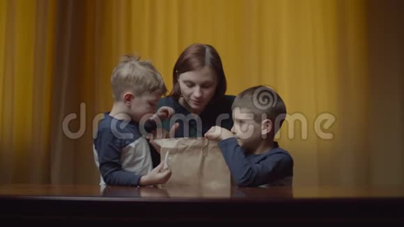 妈妈带着两个孩子打开送货包装盒和午餐快乐饥饿的家庭闻着送货包和食物视频的预览图