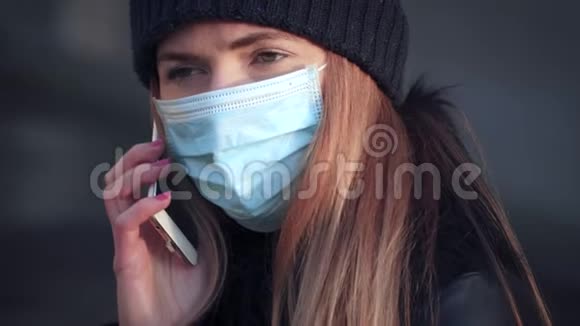 年轻女子戴一次性蓝色病毒脸口鼻罩在手机上交谈特写细节可在视频的预览图