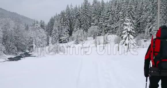 徒步旅行者背着背包走在冬天下雪的路上视频的预览图