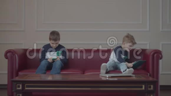 两个穿着同一件衣服的兄弟在家沙发上用小玩意小男孩躺着开始用腿打弟弟视频的预览图