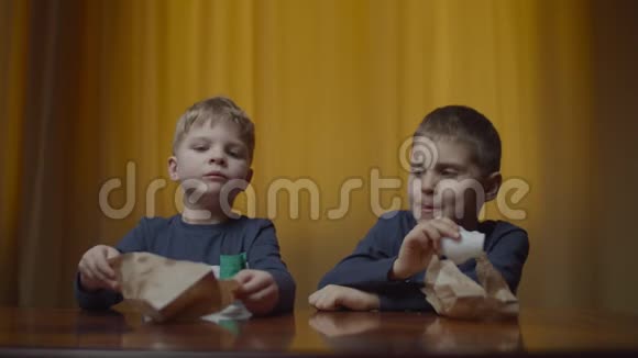 两个兄弟姐妹穿着同样的衣服在家里的桌子上吃着薯片纸袋里的食物男孩喜欢吃零食视频的预览图