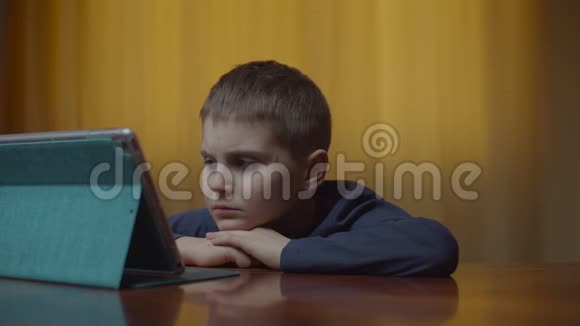 自闭症男孩使用平板电脑坐在办公桌前的肖像家里有小玩意的自闭症孩子自闭症视频的预览图