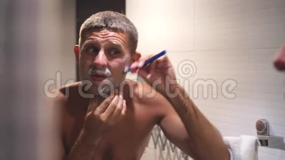 一个年轻人在镜子前的浴室里刮胡子视频的预览图