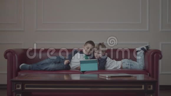 两个兄弟穿着同样的衣服用小玩意躺在家里的沙发上小兄弟在沙发上看着一台平板电脑视频的预览图