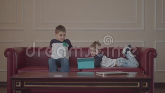 两个穿着同一件衣服的兄弟在家沙发上用小玩意小兄弟在沙发上看着一台平板电脑视频的预览图