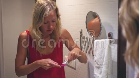年轻的金发女人正在浴室里刷牙视频的预览图