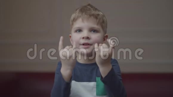 金发学龄前男孩微笑的肖像用手指显示岩石手势看着镜头年轻积极的孩子视频的预览图