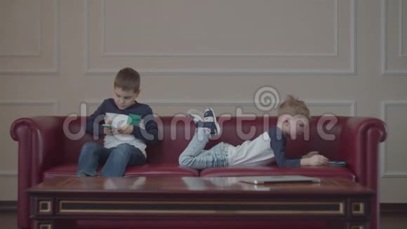 两个兄弟姐妹穿着同一件衣服使用小玩意在家里的沙发上玩耍一个男孩把手机从他身上拿走视频的预览图