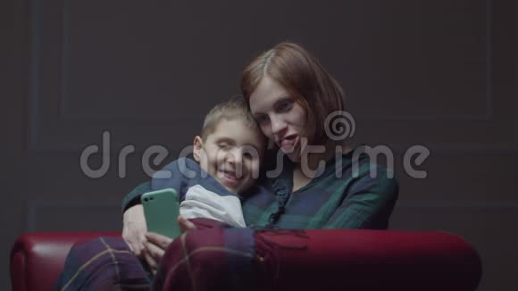 30多岁的年轻母亲带着上学的儿子使用手机坐在舒适的扶手椅上家庭在家里玩小玩意视频的预览图