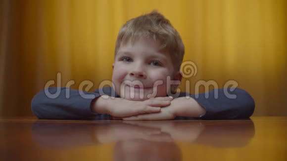 金发学龄前男孩微笑着看镜头的肖像孩子们在家里坐在桌子上微笑的孩子会竖起大拇指视频的预览图