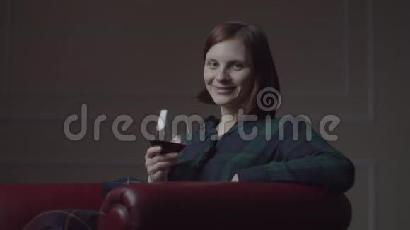 30多岁的年轻女性在家里坐在舒适的红色扶手椅上喝红酒女人独自微笑手牵手视频的预览图