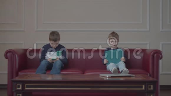 两个穿着同一件衣服的兄弟在家沙发上用小玩意小兄弟看着不同的装置坐在红色沙发上视频的预览图