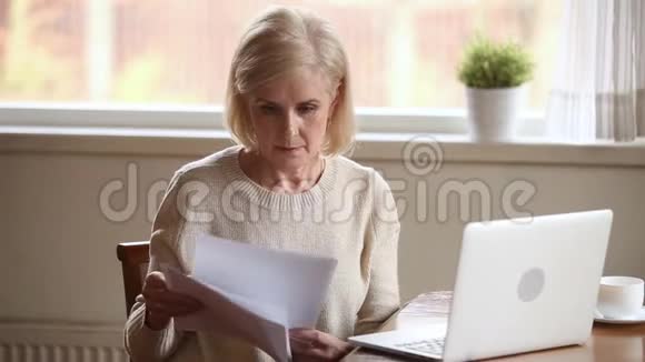 戴着帽子的高级妇女拿着被家庭账单困扰的文件视频的预览图