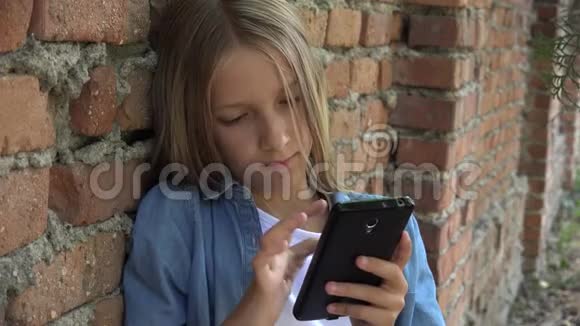孩子使用智能手机孩子玩智能手机女孩在公园户外视频的预览图