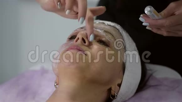 女孩美容师在客户脸上涂一种麻醉霜准备手术视频的预览图
