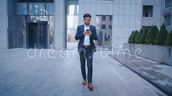年轻的商人在大城市商业区街上散步时使用智能手机穿着得体大人物视频的预览图