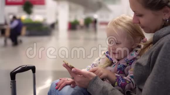 机场有个孩子的女人的肖像乘客在机场使用智能手机视频的预览图