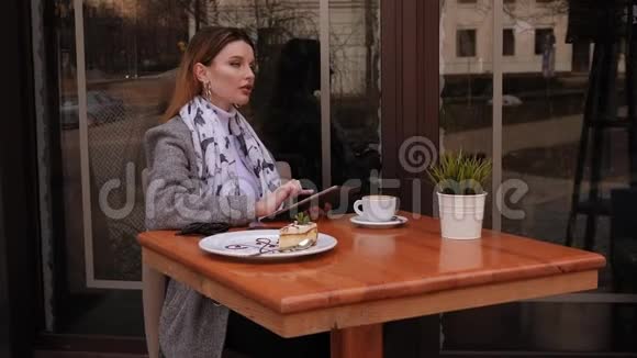一个穿外套的女孩正坐在一家带着平板电脑的街头咖啡馆里喝咖啡视频的预览图