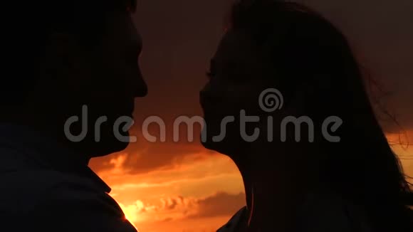 一对年轻夫妇在日落时的剪影在刮风的天气里对着红色的天空视频的预览图