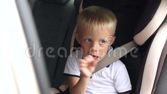 穿着白色t恤的小男孩坐在车里的汽车座椅上吃着棒棒糖视频的预览图