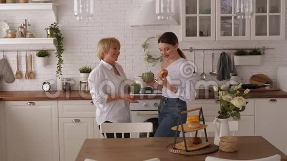 年轻女子和年迈的母亲在家中的现代厨房喝茶视频的预览图
