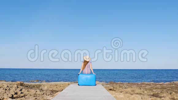 一个旅行者女人坐在沙滩上的手提箱上视频的预览图
