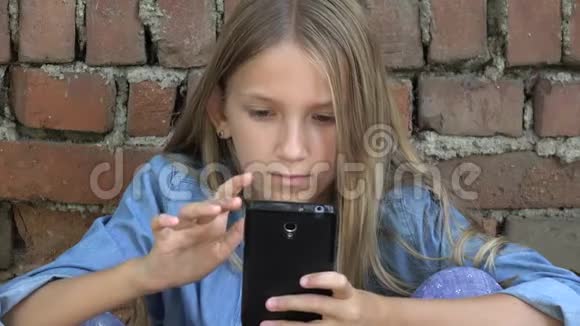 孩子使用智能手机孩子在智能手机上聊天青少年女孩在公园户外上网视频的预览图