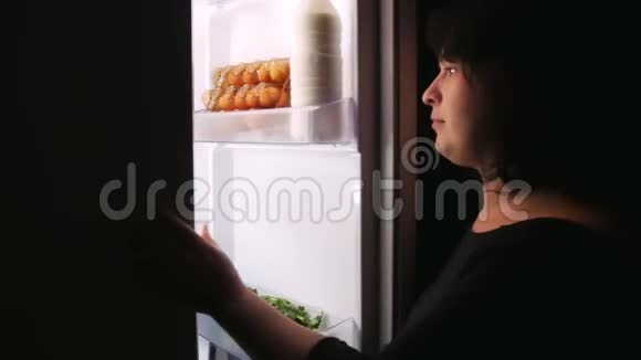 一个女人从冰箱里得到一个纸杯蛋糕打开并关闭冰箱门视频的预览图