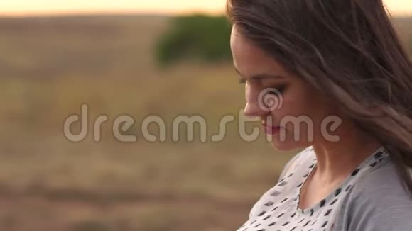一个年轻女孩的肖像长发在夕阳下的一片田野里在大风中视频的预览图