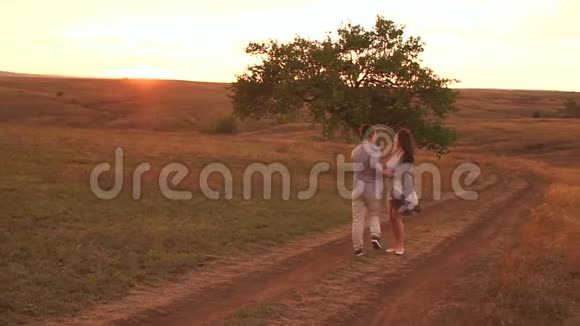 一位孕妇和她的丈夫正在日落时沿着一条乡村道路散步视频的预览图