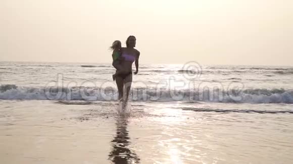 一个女人带着一个孩子在阳光的背景下从大海中走出来视频的预览图