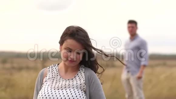 美丽的孕妇长着棕色的头发在日落时站在田野里视频的预览图