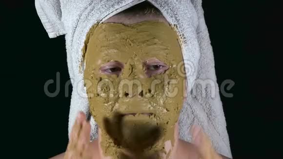 头上戴海藻酸钠面具和毛巾的女孩用手摸她的脸视频的预览图