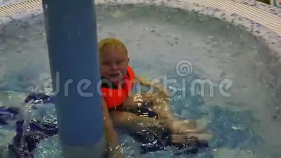 穿着救生衣的小男孩坐在划水池里在滴水之上视频的预览图
