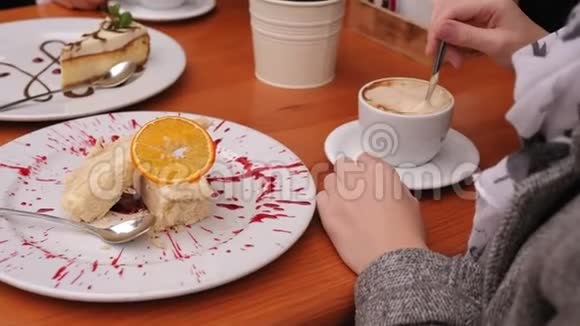 一个女孩在街头咖啡馆里用一杯卡布奇诺和一个蛋糕她的手视频的预览图