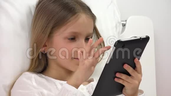 儿童在床上玩平板电脑儿童在触摸屏智能手机上浏览互联网女孩肖像不在电脑上放松视频的预览图