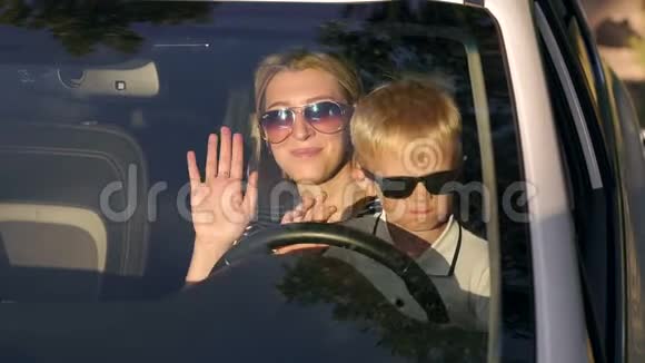 一位年轻的母亲和她的儿子戴着太阳镜在夕阳下的汽车上的肖像视频的预览图