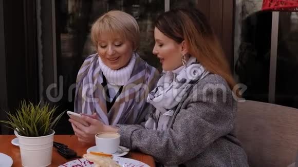 老年妇女和她的成年女儿使用智能手机在咖啡馆喝咖啡视频的预览图